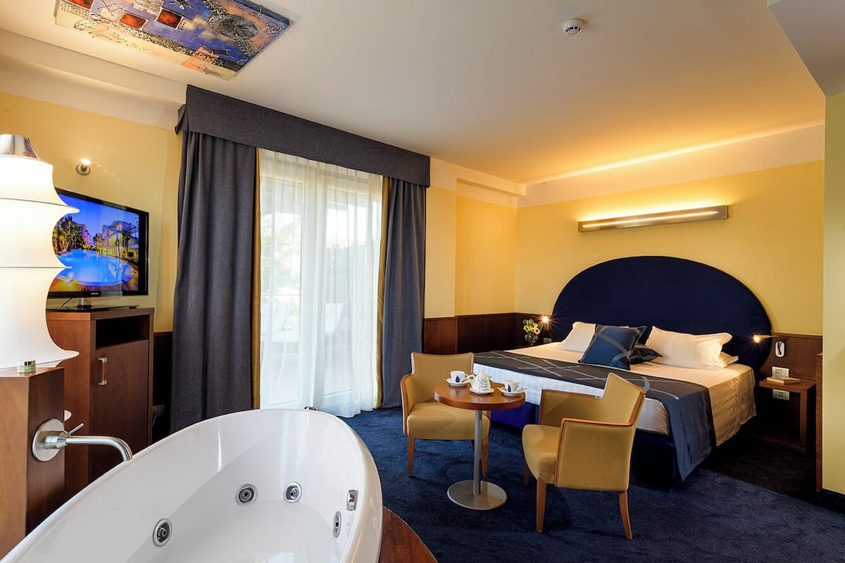 Ein Hotelzimmer mit einem großen Bett, einer Sitzecke mit Tisch und Stühlen, einem Fernseher und einer Badewanne.