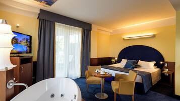 Una habitación de hotel con una cama grande, una zona de estar con una mesa y sillas, un televisor y una bañera.
