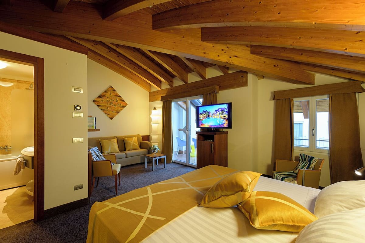 Ein Hotelzimmer mit Holzboden, einem Bett mit gelber Bettwäsche, einem Fernseher, einem Sofa und einem kleinen Tisch.