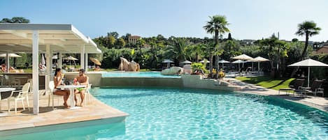 A pool area with lounge chairs and umbrellas, a covered seating area, and a view of a residential area in the background.