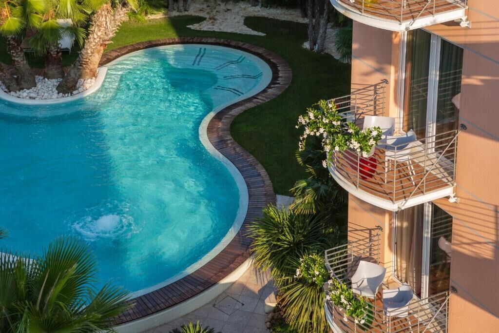 A swimming pool with a curved edge, surrounded by a landscaped area with palm trees and a small island.