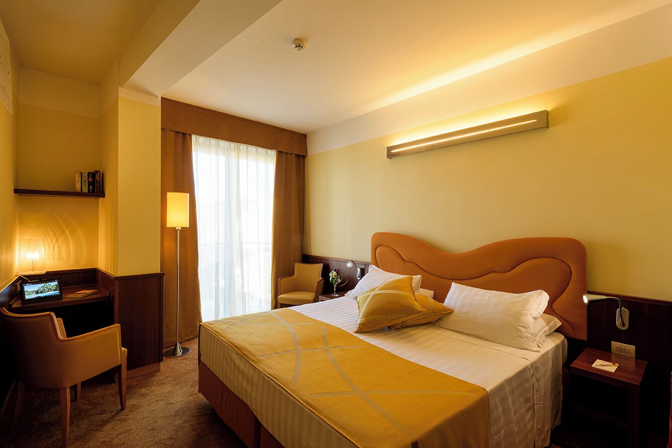 A hotel room with a bed, desk, chair, and bedside table.