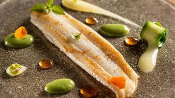 A dish with a piece of white fish, green vegetables, and a sauce on a textured surface.