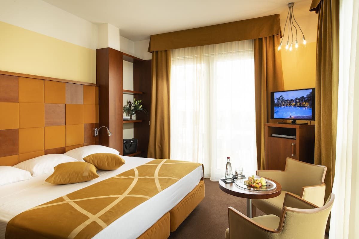Ein Hotelzimmer mit einem großen Bett, einem Fernseher, einem kleinen Tisch mit Obstplatte und einem Sessel.
