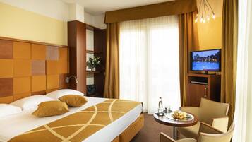 Habitación de hotel con una cama grande, televisión, una mesita con una bandeja de frutas y una silla.