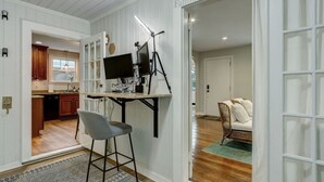 A room with a desk, chair, and a view of a kitchen and living area.