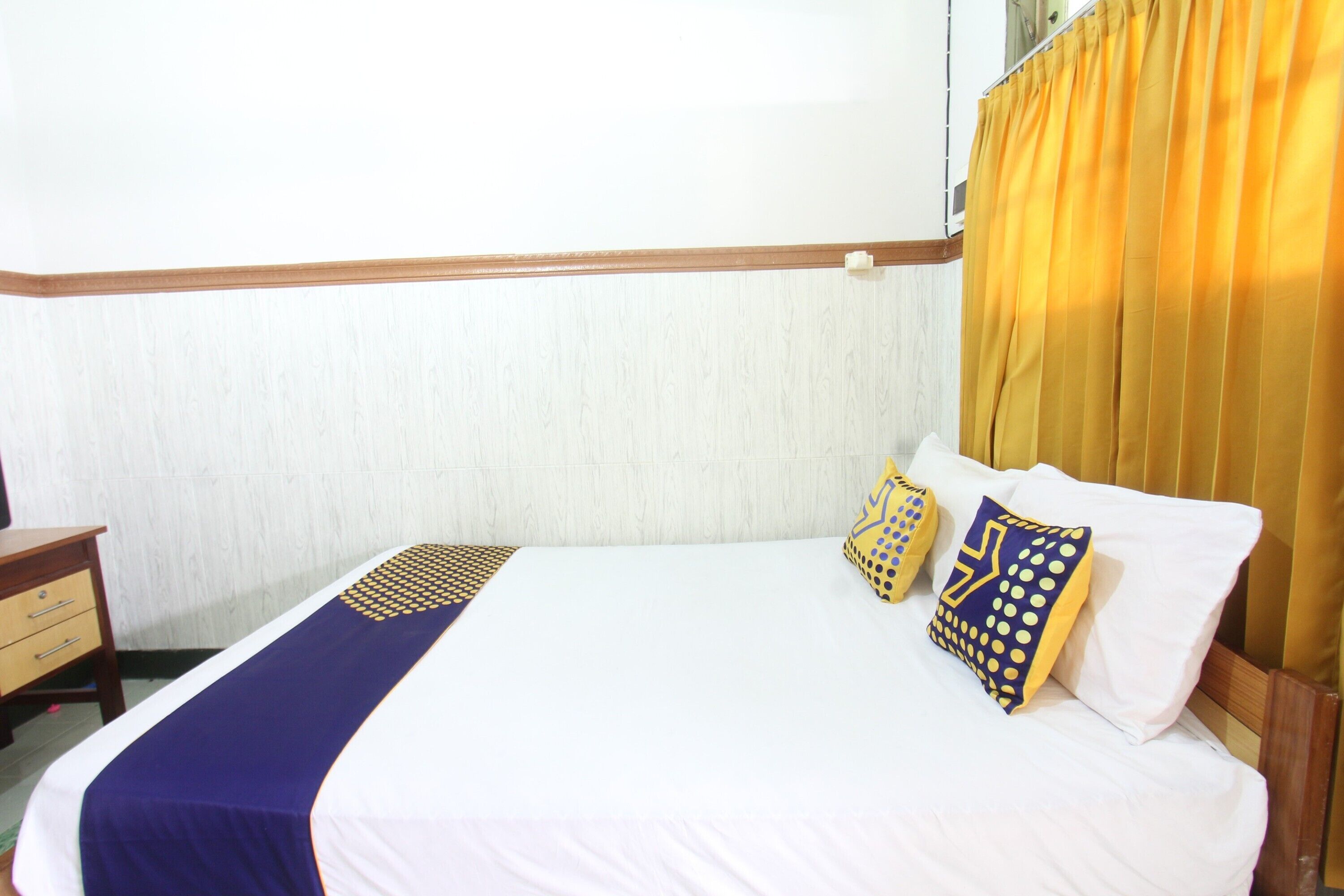 Une chambre d’hôtel avec un lit, une table de chevet et une fenêtre avec des rideaux jaunes.