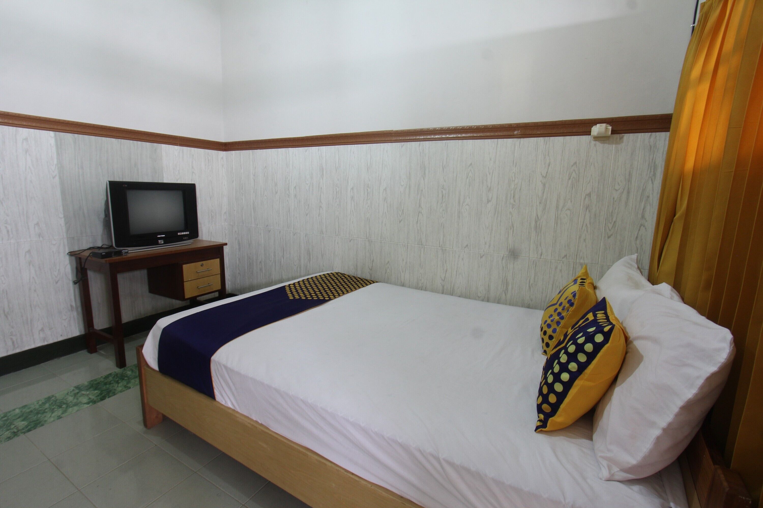 A bedroom with a bed, a TV on a wooden desk, and a curtain.