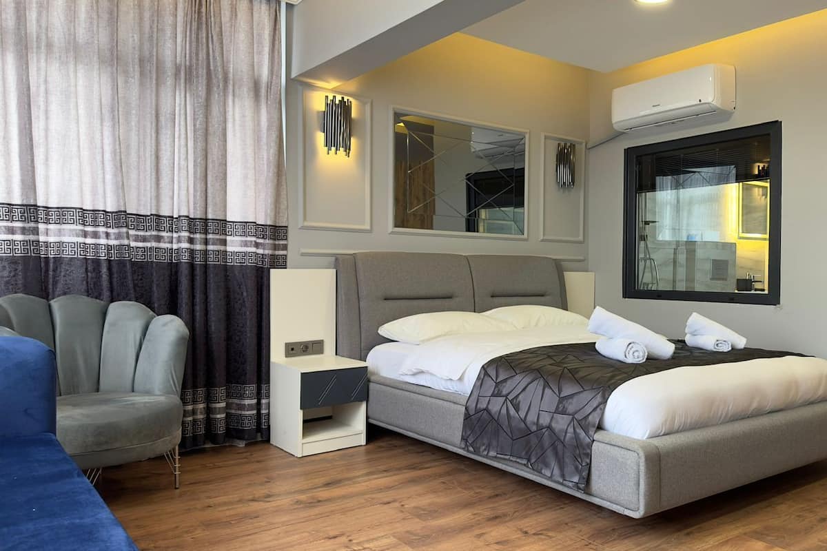Une chambre d’hôtel moderne dotée d’un grand lit, d’une table de chevet, d’une armoire et d’un coin salon avec un fauteuil.