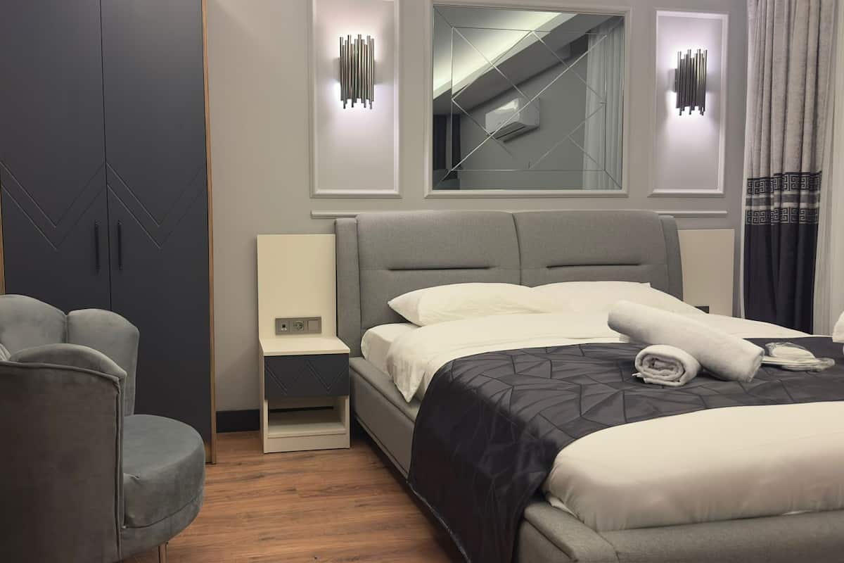 Une chambre d’hôtel moderne, équipée d’un lit, de deux fauteuils, d’une table de chevet et d’un miroir.