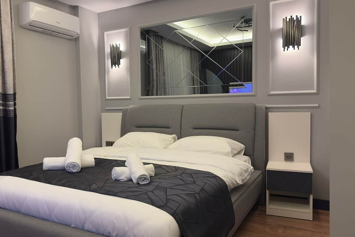 Une chambre d’hôtel moderne avec un grand lit, des murs gris et un miroir au-dessus du lit.