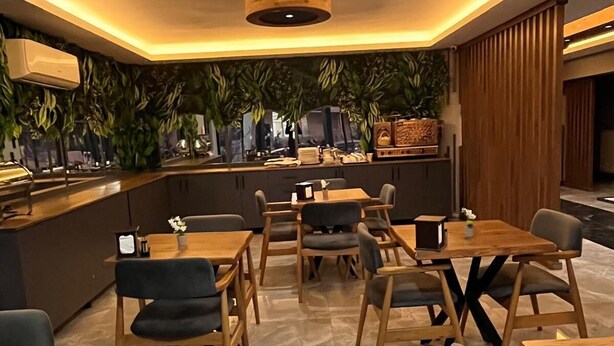 A modern restaurant with wooden tables and chairs, a bar area, and green plants on the walls. - Wonne Boutique Hotel (Ankara)
