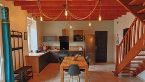A modern kitchen with wooden cabinets, a large island, and a dining area with a wooden table and chairs. - Stone house 3km from the beach and close to all amenities. (Penvénan)