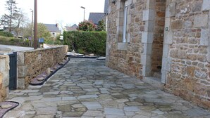 A stone-paved alleyway between buildings with a stone wall on one side and a window on the other. - Stone house 3km from the beach and close to all amenities. (Penvénan)