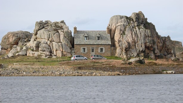 A house built into a rocky cliffside with two cars parked in front. - Stone house 3km from the beach and close to all amenities. (Penvénan)