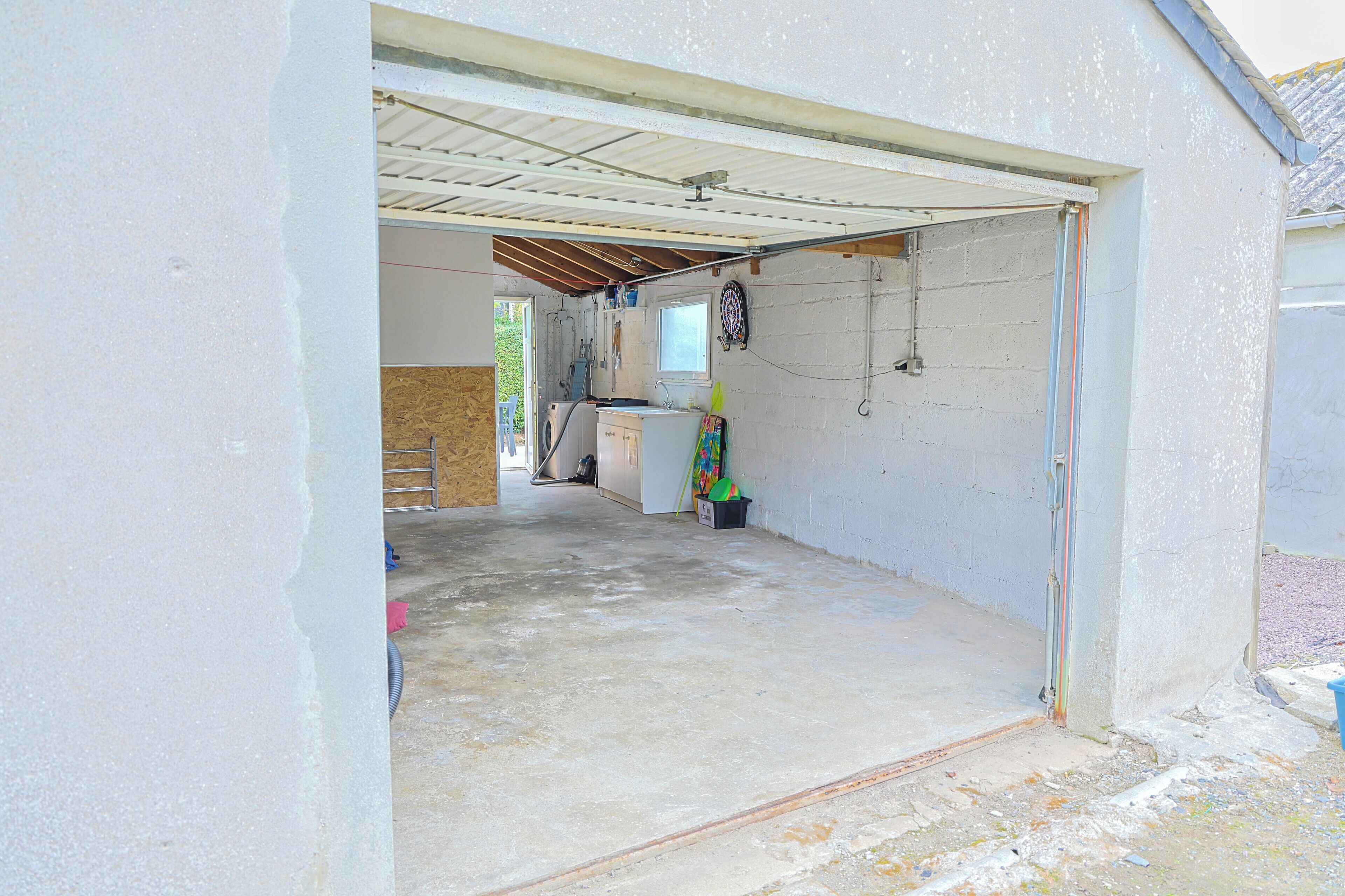 A garage with a concrete floor, a white wall, and a metal roof.