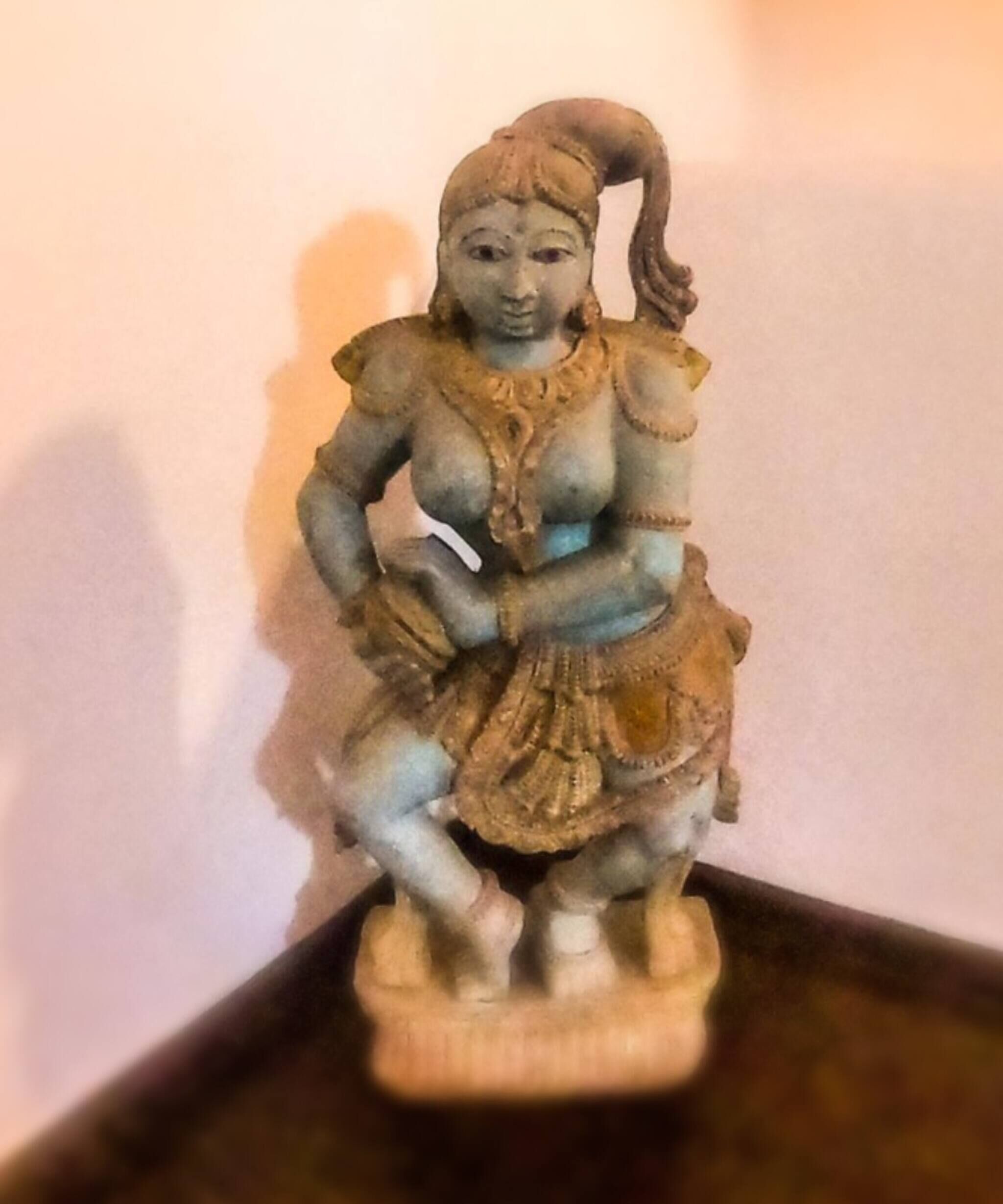 Een standbeeld van een figuur met arm omhoog en een gebogen voorwerp in de hand, op een voetstuk.