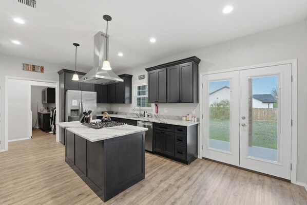 A modern kitchen with a central island, dark cabinetry, and a view to the outside.