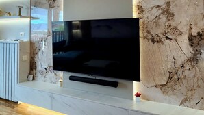 Una sala de estar moderna con un televisor de pantalla plana grande montado en una pared de mármol, piso de madera y un mueble blanco minimalista.