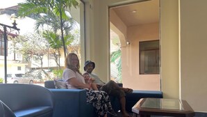 A seating area with a sofa and a glass-top table, a large window with a view of the street, and a door leading outside. - Rani Beach Hotel (Negombo)
