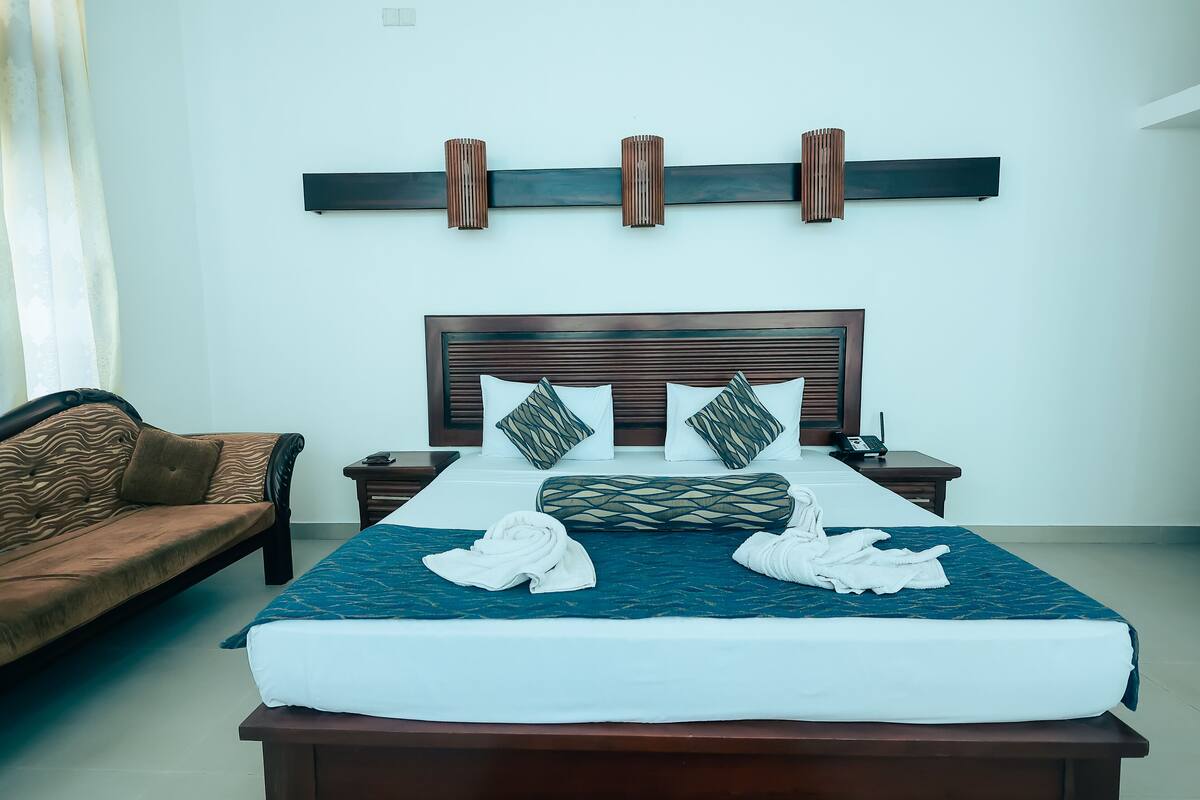 A neatly made bed with a blue quilt, a brown sofa, and a wooden headboard.