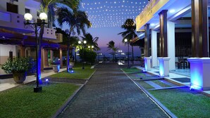 A pathway lined with palm trees and potted plants, leading to a building with columns and a covered area. - Rani Beach Hotel (Negombo)