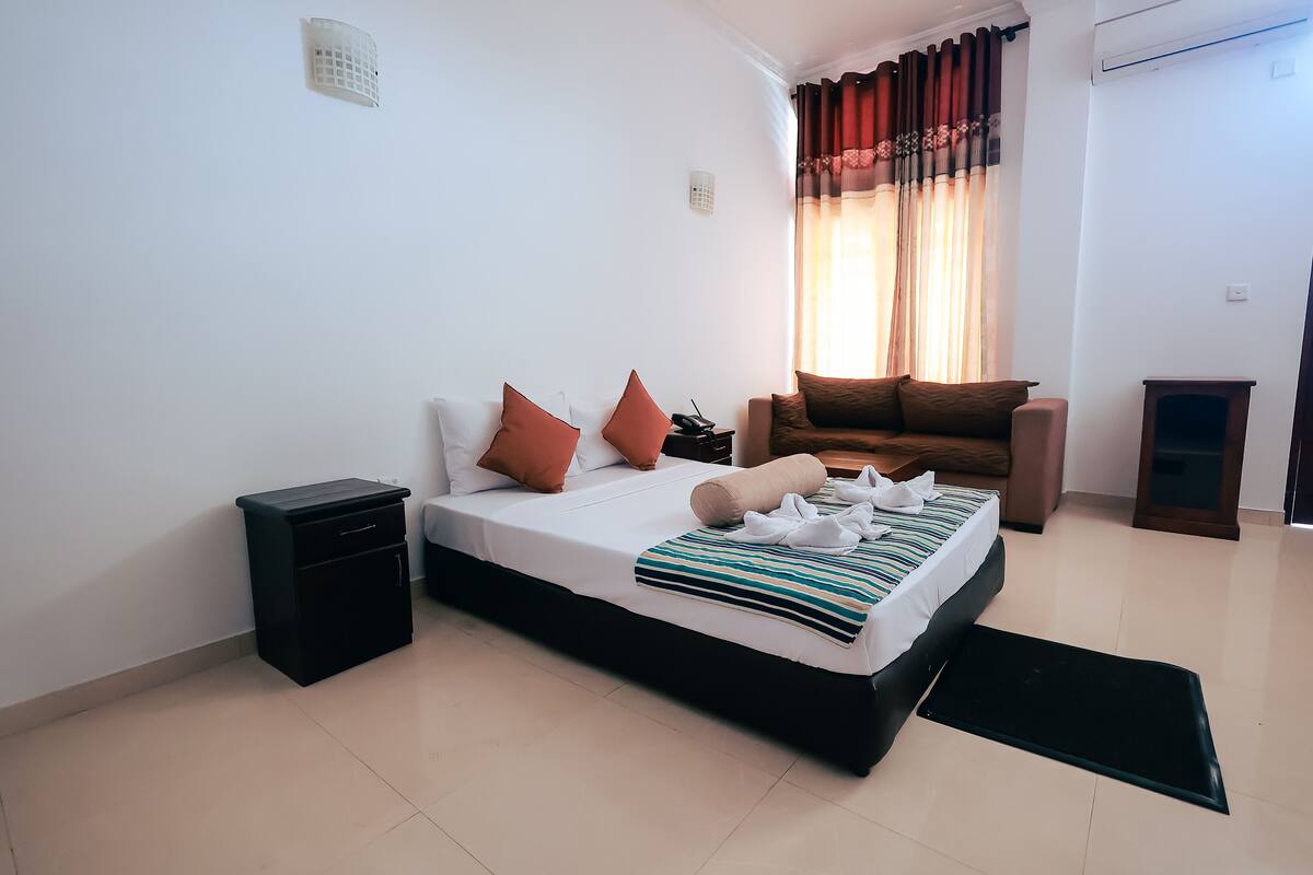 A neatly arranged bedroom with a bed, bedside tables, a small cabinet, a sofa, and a window with curtains.