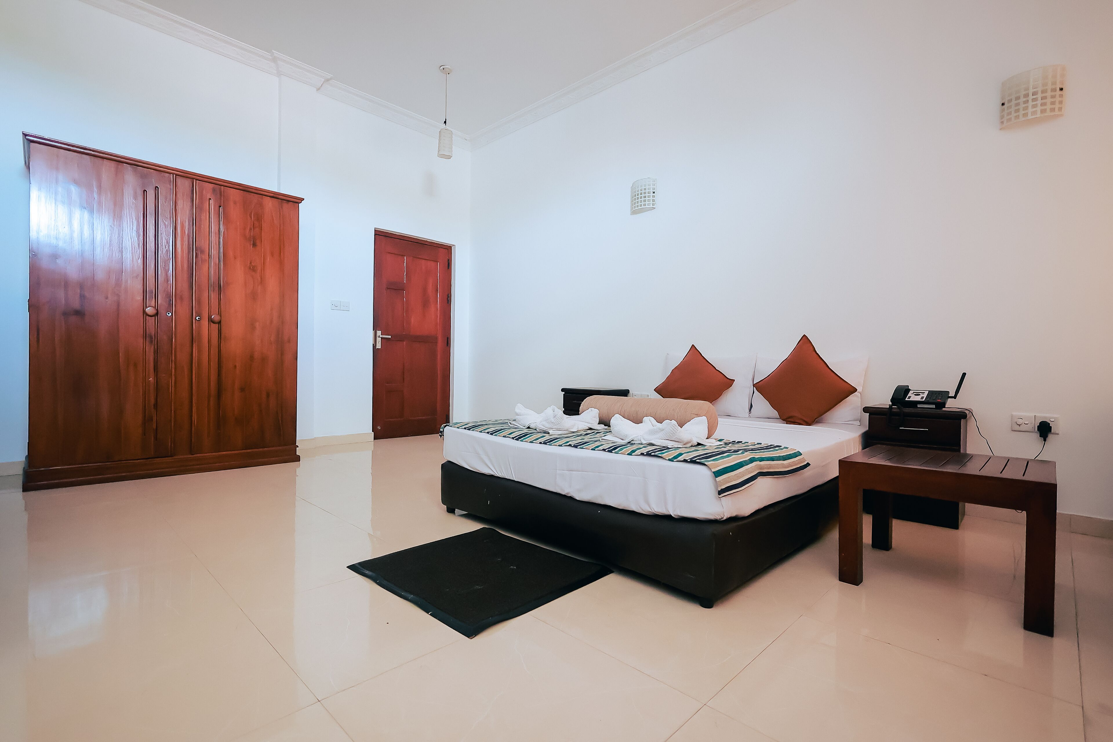 A bedroom with a bed, a nightstand, a wooden wardrobe, and a black mat.