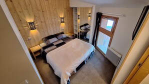 A bedroom with a wooden slat wall, a bed with a white blanket, and two wall-mounted lights. - Appart Duplex / La Plagne, Montchavin / 3 Chambres, 8 Pers / Pied des Pistes (La Plagne-Tarentaise)