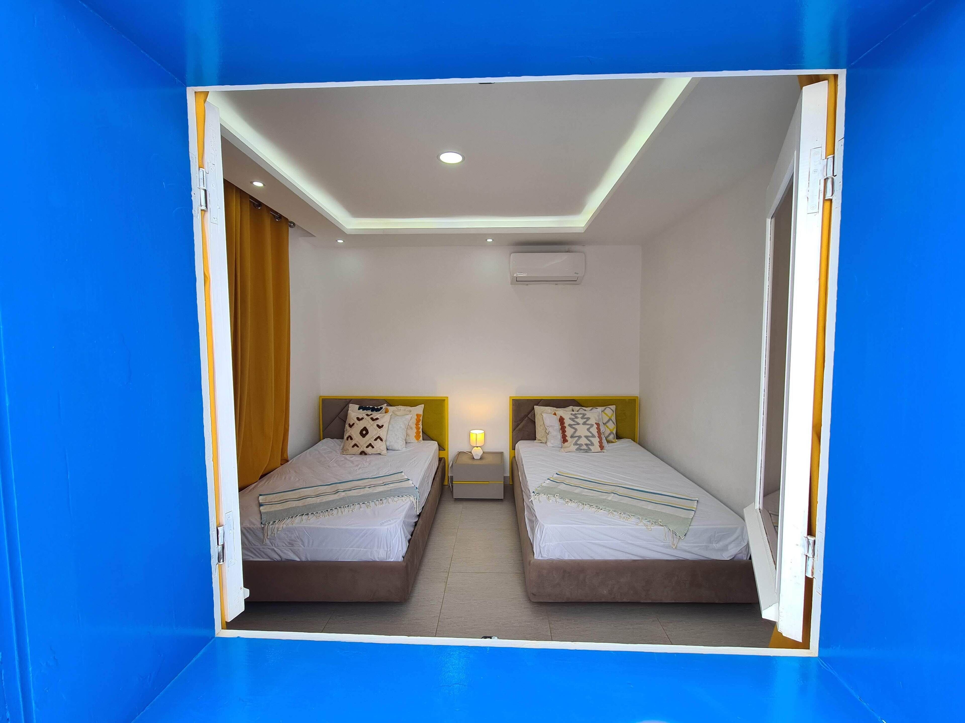 Een kamer met twee bedden, een nachtkastje met een lamp en een airconditioning aan de muur.