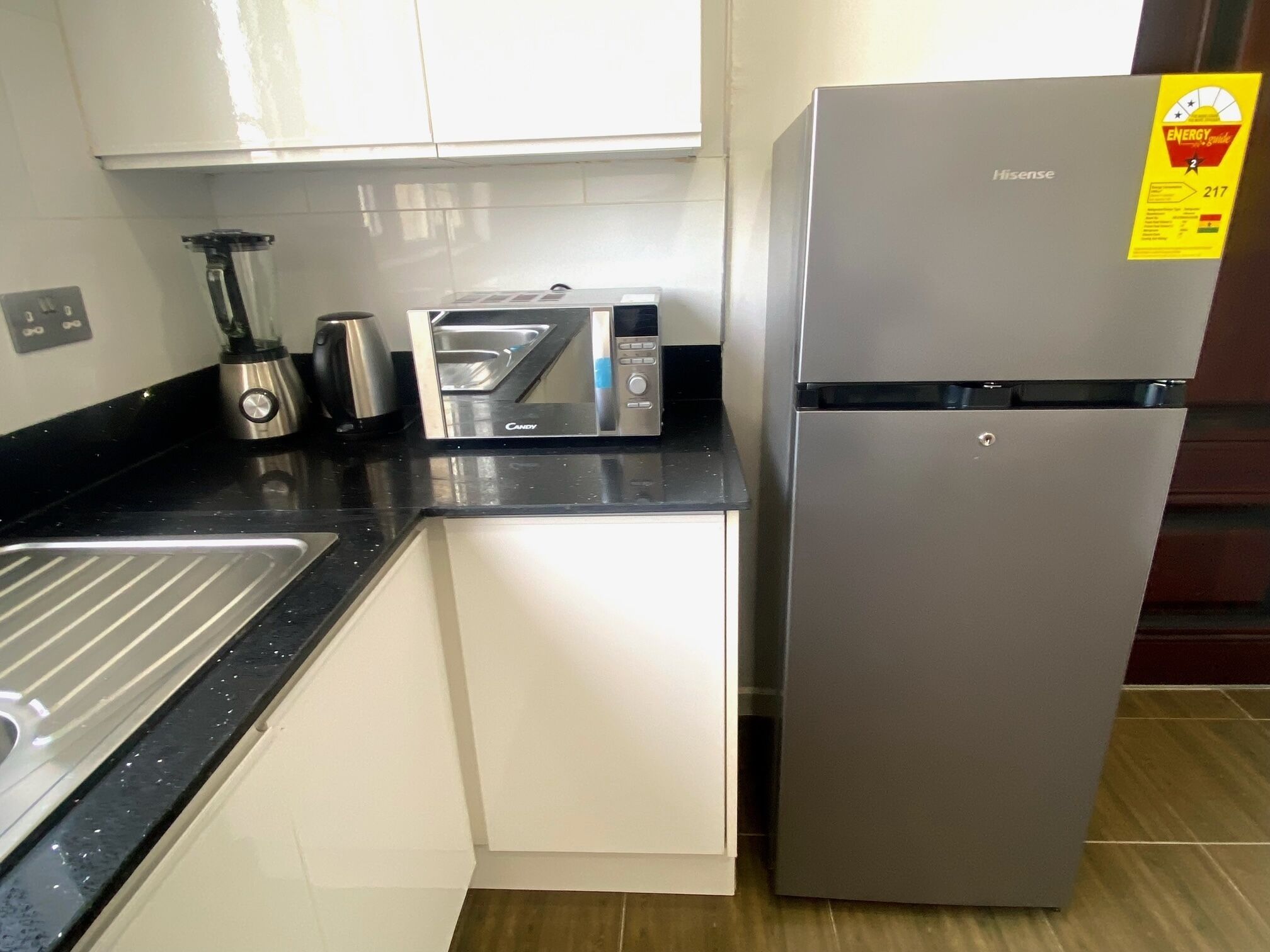 Una cocina compacta con un refrigerador de acero inoxidable, un microondas, un tostador y una licuadora sobre la encimera.