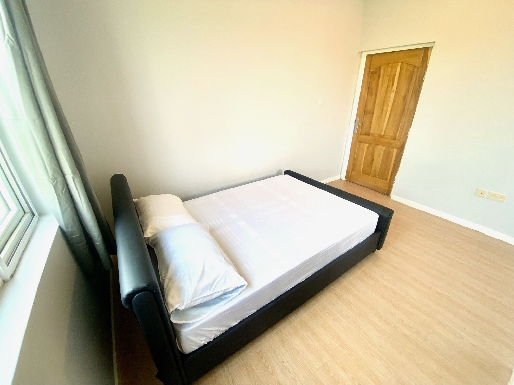 A single bed in a room with a wooden floor and a door in the background.