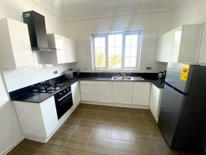 A modern kitchen with white cabinets, a black countertop, a gas stove, a sink, and a refrigerator. - Sanctuary House Apartments (Santeo)