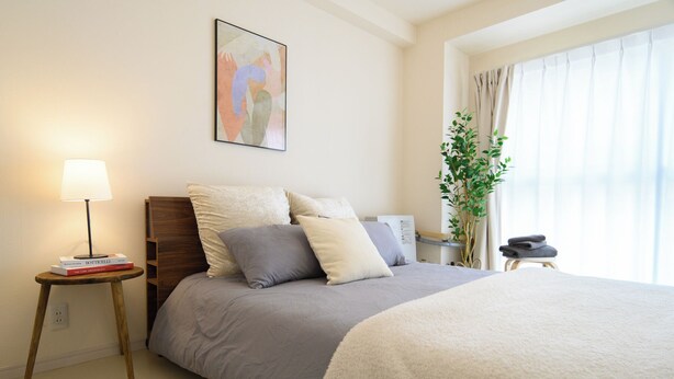 Una camera da letto ordinata con un letto, un comodino, una lampada e una pianta.