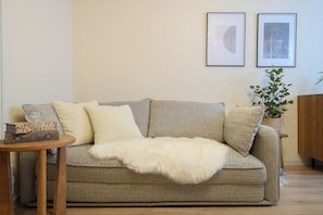 Una sala de estar con un sofá gris, un plaid blanco esponjoso y dos cuadros en la pared.