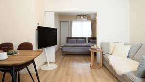 Una moderna camera d'albergo con televisione a schermo piatto montata a parete, un tavolo da pranzo in legno con sedie, un divano e un letto con testiera in legno.