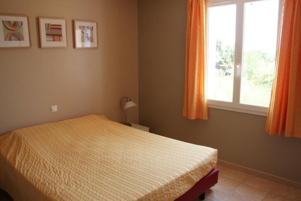 Une chambre à coucher avec un lit, une fenêtre avec des rideaux et trois tableaux encadrés accrochés au mur.