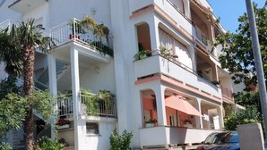 Un edificio de varios pisos con balcones, plantas en macetas y un coche estacionado.