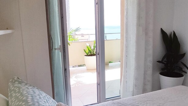 Un dormitorio con cama, una puerta corrediza de vidrio que da a un balcón y una planta en maceta.
