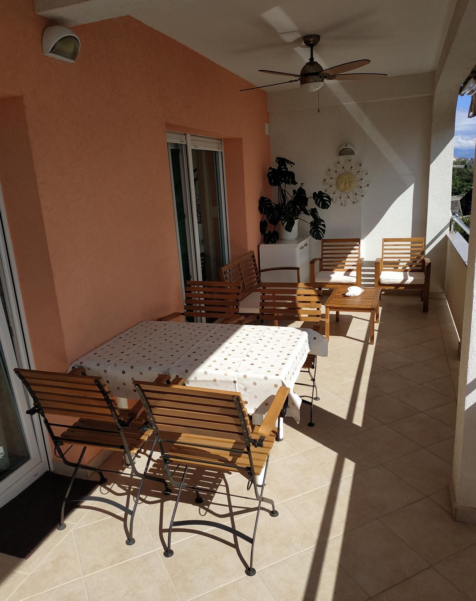 A sunlit outdoor patio with a table and chairs, a ceiling fan, and a potted plant.