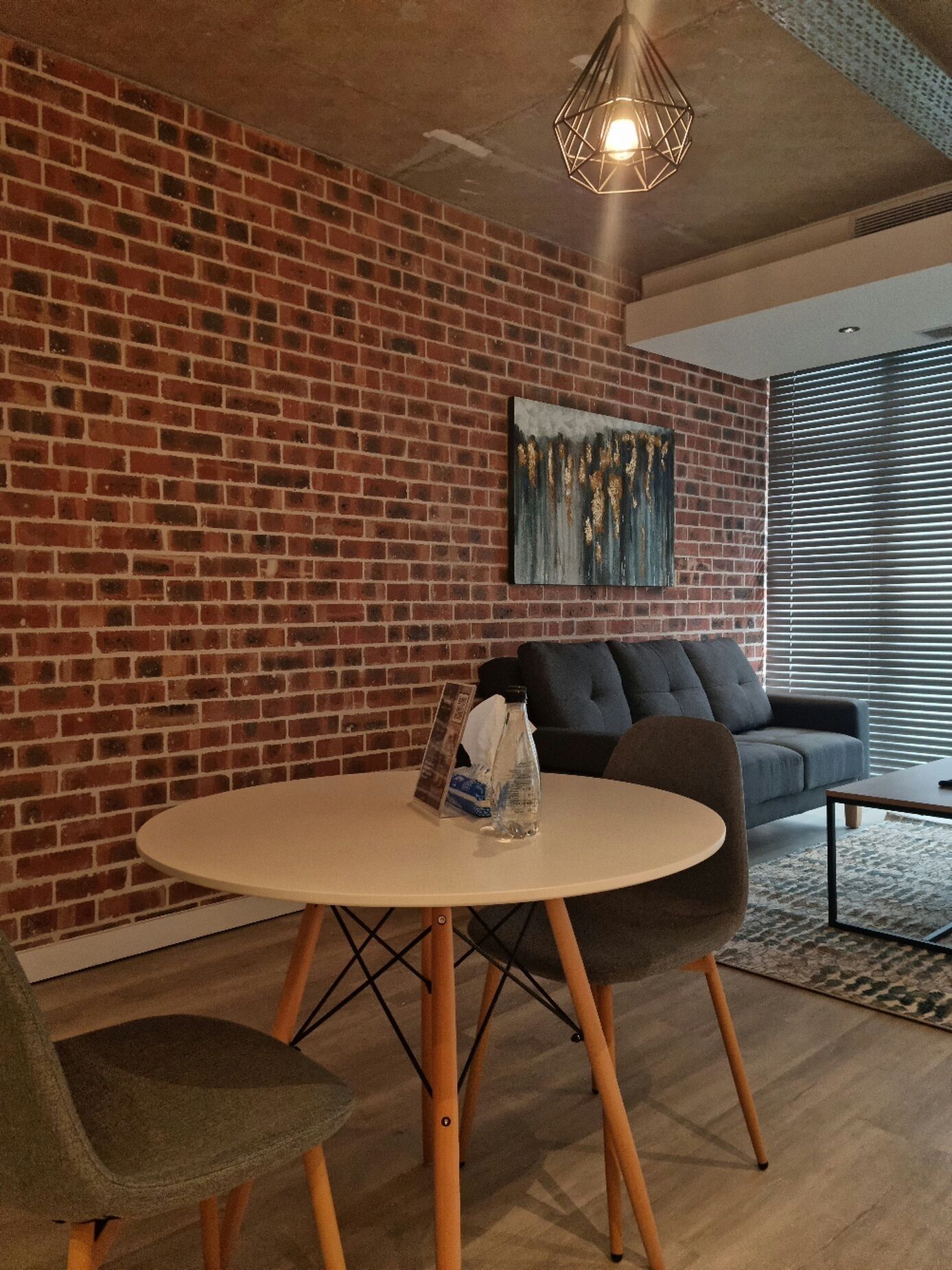 A modern room with a brick wall, a round table with chairs, a sofa, and a painting.