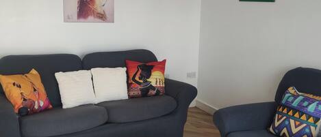 Un salón con un sofá gris oscuro, una mesa de centro blanca y cojines coloridos.