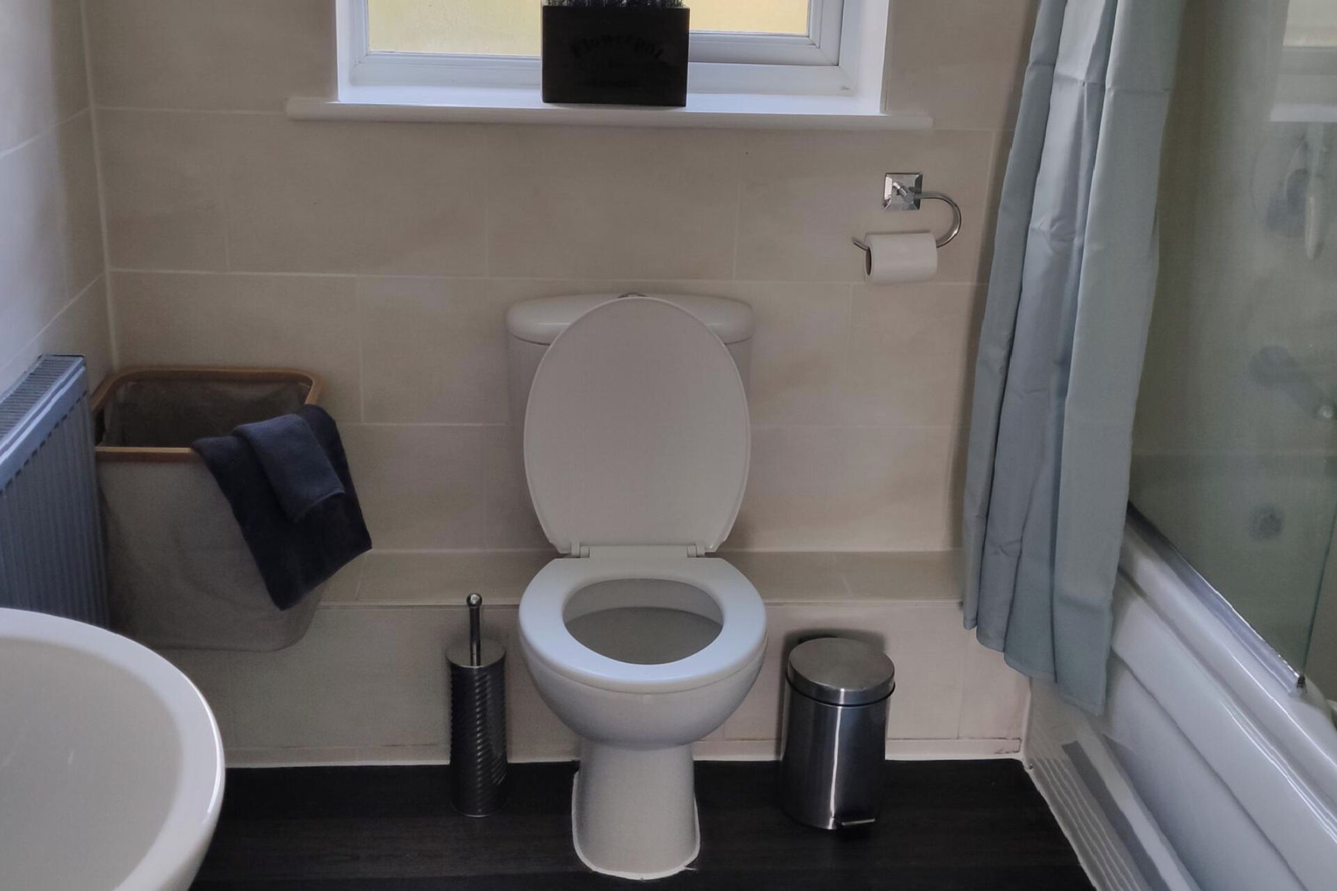 Une salle de bain comprenant des toilettes, une poubelle, un porte-serviettes et une fenêtre située au-dessus des toilettes.