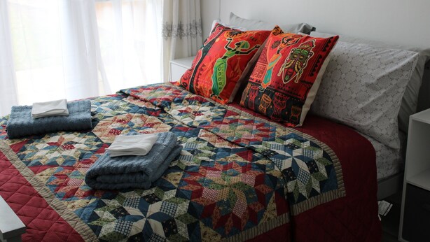 Un lit bien fait, recouvert d’une courtepointe aux couleurs vives, avec deux oreillers aux motifs complexes et des serviettes pliées posées sur le lit.