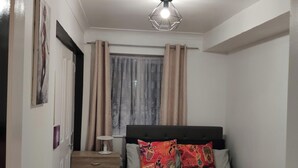 A bedroom with a bed, a bedside table, a lamp, a window with curtains, and a door. - Stunning 2-bed Apartment in London Dagenham (Dagenham)