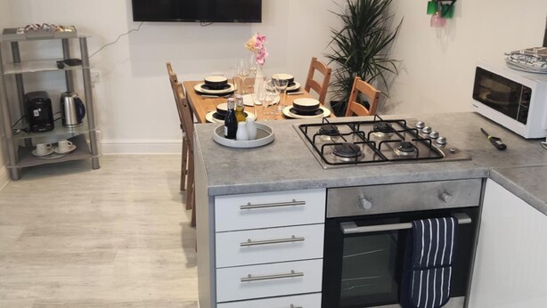 A modern kitchen with a gas stove, oven, and a coffee machine on a shelf. - Stunning 2-bed Apartment in London Dagenham (Dagenham)
