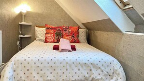 Une chambre avec un plafond en pente, un lit avec une literie à motifs, deux oreillers à carreaux rouges et noirs, et une lampe de chevet.
