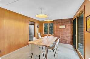 Un coin repas avec une table et des chaises en bois, un réfrigérateur et un mur en briques.