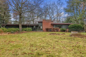 Une maison moderne à deux étages, dotée d’une cheminée en briques, d’une pelouse bien entretenue et de grands arbres.