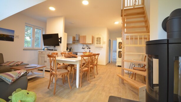 A spacious living area with a dining table, chairs, a sofa, a television, and a staircase leading to an upper level. - Fewo 4 Triftweg 10 (Loddin)